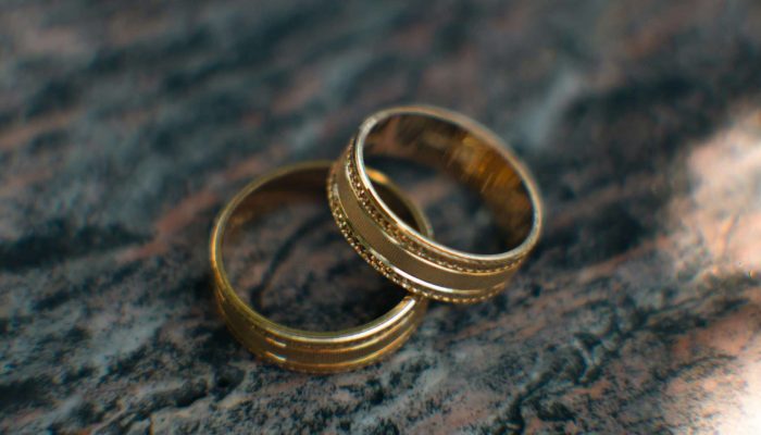 Two gold wedding bands with textured designs overlap on a marbled surface